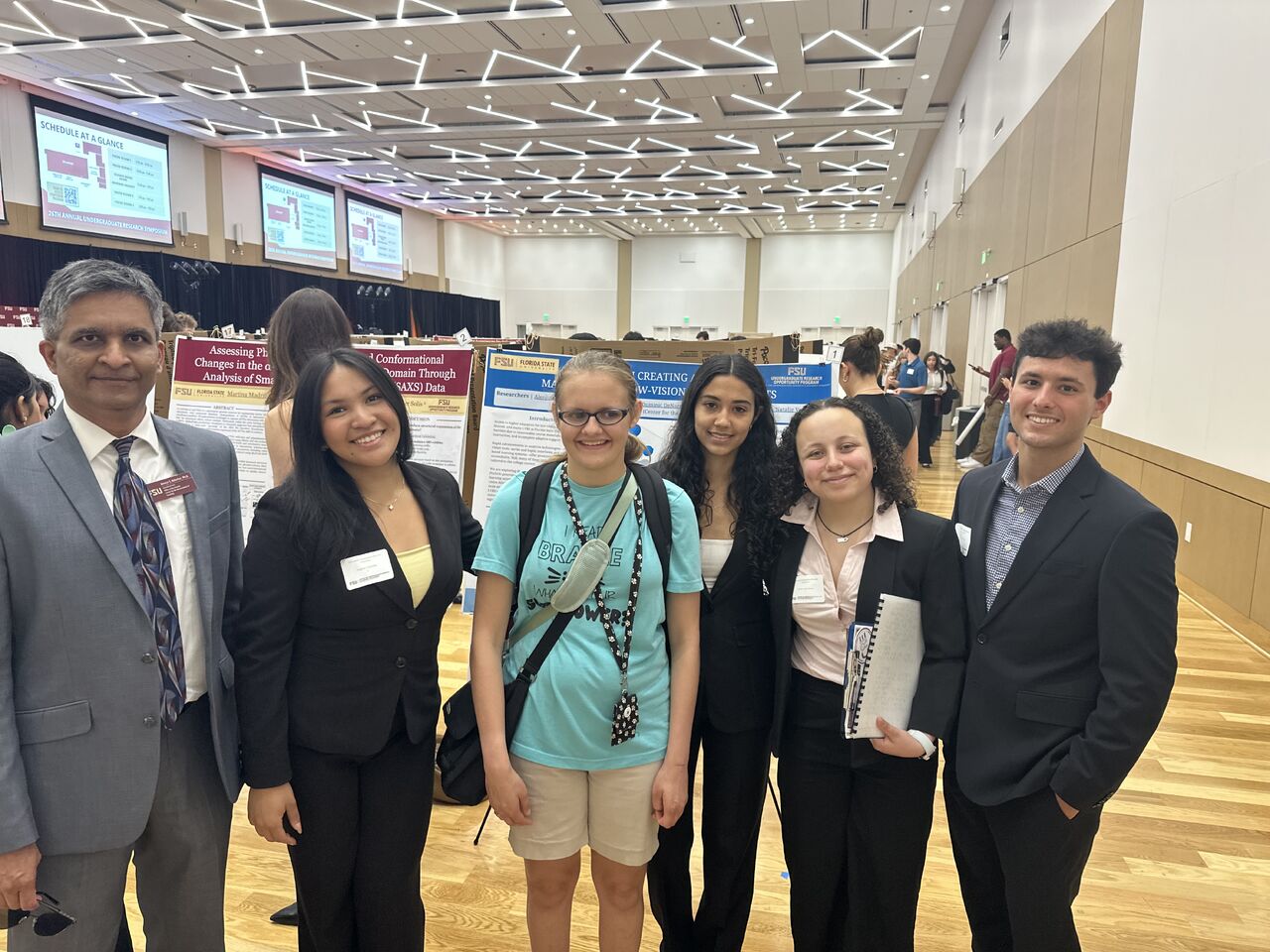 4 of 6 research students presenting at the poster session. Our blind student research assistant is standing third from the left. They are standing in front of the poster with their mentor, Dr. Kolarkar, standing at the far left.